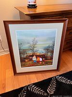 Full view of the framed print leaning against a dresser on wooden floor with a small ceramic piece on the dresser visible.