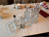 Crystal glassware lot on table including four etched decanters with stoppers, salt and pepper shakers, tray, and small bowls.