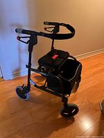 Photo showing Nexus walker with padded seat, storage basket, three wheels, and adjustable handles in an indoor setting with wooden floor.