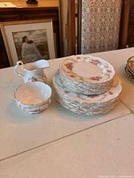 Stacked bone china plates showing floral pattern and gold trimmed scalloped edges, milk jug and sugar bowl placed beside plates.