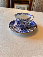 Blue and white Royal Crown Derby Mikado tea cup and saucer set on white tablecloth, showing intricate pattern and gold trim.