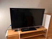 Front view of the Sony KDL-40EX500 40-inch LCD TV showing the screen, original remote on the stand, and two small external speakers.