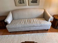Front view of light grey upholstered sofa showing curved backrest, rolled armrests, and single seat cushion. Wooden legs visible.