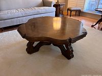 Side angle view showing scalloped edges and carved wooden legs of the square coffee table.