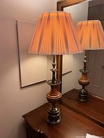 Lamp lit, showing warm glow through pleated fabric shade and brass base reflecting in mirror.