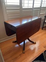 Side angled view of table with right drop leaf down, showing the table top, drawer, pedestal base and claw foot brass toes.