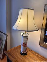 Lamp turned on, showing warm light with white fabric shade and decorative porcelain base with red designs.