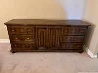 Front view of vintage solid wood dresser showing six drawers and central carved cabinet doors.