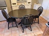 Photo showing the wood grey oval kitchen table with 4 matching spindle-back chairs, with table leaves inserted.