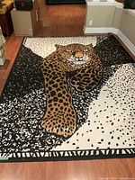 Full view of large area rug laid on hardwood floors showing a detailed image of a stretching leopard in the center with an abstract black and beige spotted pattern around.