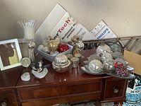 Wide view of assortment of vintage Christmas decorations including glass balls in metal trays on wood cabinet with candle holder, photo frame, and penguin figurines