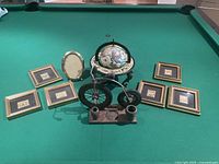 Overview of decorative items on pool table showing six small framed landscape prints, an oval frame, and a decorative globe bicycle stand with candle holders.