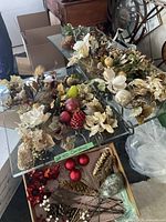Glass shelf display of assorted Christmas picks including faux apples, pomegranates, white flowers, and gold leaves with various berries and decorative elements.