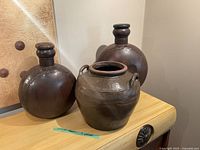 Three large decorative pots on display - two metal with wooden tops and one clay pot with handles