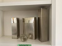 Three rectangular stainless steel vases and a clear glass paperweight ball arranged on a shelf