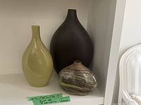 Three ceramic vases displayed on a white shelf, showing size comparison and colors.
