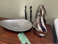 Photo showing entire lot arranged on wooden surface including two metal vases, large metal display bowl, and two carved statues.