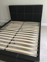 Photo showing the full structure of the unassembled double bed frame with black faux leather upholstery and wooden slats for mattress support.