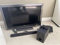 Sony Bravia TV, Phillips soundbar, subwoofer, and Samsung DVD player with remotes and cables on carpeted floor.
