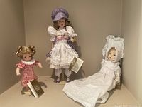 Three Franklin Heirloom Dolls displayed together against a beige wall; woman doll at back, baby doll on right, child doll on left.