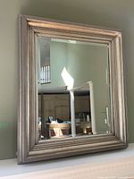 Full view of large rectangular mirror with silver metallic multi-layered frame hung on green wall showing reflected room.