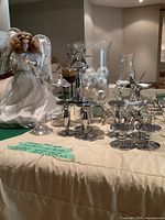 Full lot showing angel figurine, three silver metal star candle holders, two glass hurricanes with Christmas ornaments inside.