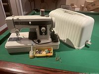 Janome Deluxe Zig Zag sewing machine with carrying case and accessories on green surface.