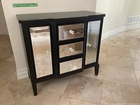 Front angle view of the black wooden hall table with mirrored drawer fronts and doors, clear crystal knobs visible.