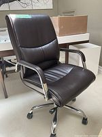 Front and side view of brown office chair showing padded seating area, armrests, and chrome metal base with wheels on carpet.