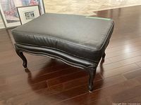 Front diagonal view of the espresso brown ottoman showing padded top and carved legs.