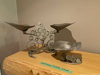 Double and single metal candle holders with swirl and circular metal decorations, silver finish, placed on wooden surface.