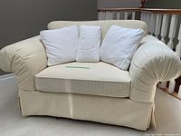 Front view of oversized butter-colored upholstered armchair with three white cushions placed on seat.