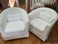 Front view of both white tub chairs on hardwood floor with staircase and storage boxes in background