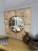 Square textured beige wall art with a large circular mirror in the center showing room reflection and decorative dark circular dots and swirls.