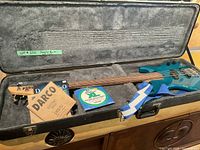 Overall view of open hard shell case with blue electric bass guitar, string packs and strap inside