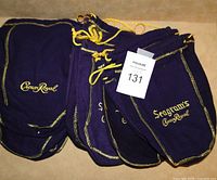 Set of 16 purple fabric drawstring bags with gold embroidered logos for Crown Royal whisky bottles.