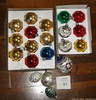 Top view showing assorted gold, red, green, blue, and yellow round Christmas ornaments in white trays with some textured and painted ornaments below