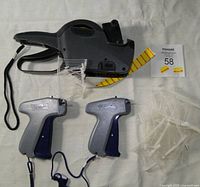 Two Laser II pricing guns silver and blue, black Garvey tag pricing gun, roll of yellow and red pricing stickers, and numerous clear plastic tag holders.