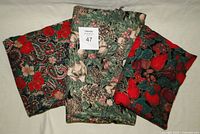 Three pieces of folded Christmas themed fabric with floral and fruit patterns and gold accents.