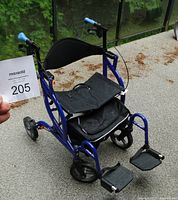 Front-left perspective of blue rollator configuration showing padded seat, basket, front wheels and footrests deployed