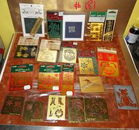 Photo showing all 21 brass embossing stencils laid out on table, some still sealed and some opened, mainly Christmas and holiday-themed patterns.
