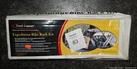 Photo of crushed white box with red, black and yellow branding showing Truck Luggage Expedition Bike Rack Kit label and some product usage images.