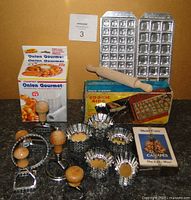 Photo showing the two ravioli presses, wooden rolling pin, six wooden handled ravioli cutters, Starfrit Onion Gourmet onion flower maker in box, Cookie King cookie press in box, canape makers, and petite four pans arranged on a counter.