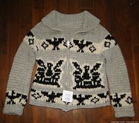 Front view of the gray hand knit Cowichan sweater with black Thunderbird and geometric pattern, showing full metal zipper and shawl collar.