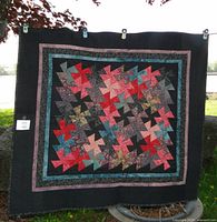 Front view of the quilt showing colorful geometric pinwheel patchwork in navy, turquoise, reds, and blues with dark borders.
