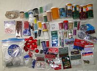 Photo showing many jars and small containers filled with assorted beads and glitter in various colors, plus craft embellishments and buttons spread on a surface.