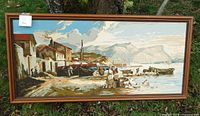 Full view of the vintage wool needlepoint art depicting a seaside village, framed in wood.