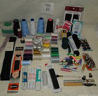 Lot of assorted sewing notions including thread spools, needles, pins, measuring tape, zipper packs, elastic bands, and small tools.
