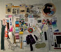 Photo showing large assortment of sewing notions including thread spools, buttons, zippers, trims, snaps, and eyelets