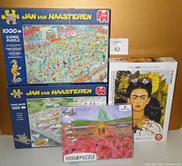 Photo showing four puzzle boxes: two Jan van Haasteren comic puzzles, one Frida Kahlo fine art puzzle, and one Wizard of OZ puzzle unopened in packaging.